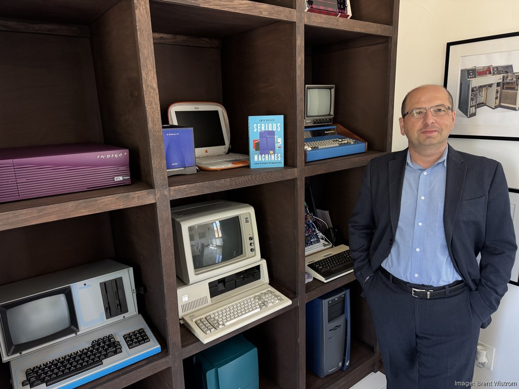 Amir Husain beside the collection shelves, with an SGI Indigo2, a Cobalt Qube, an IBM PC and a Commodore 64 behind him